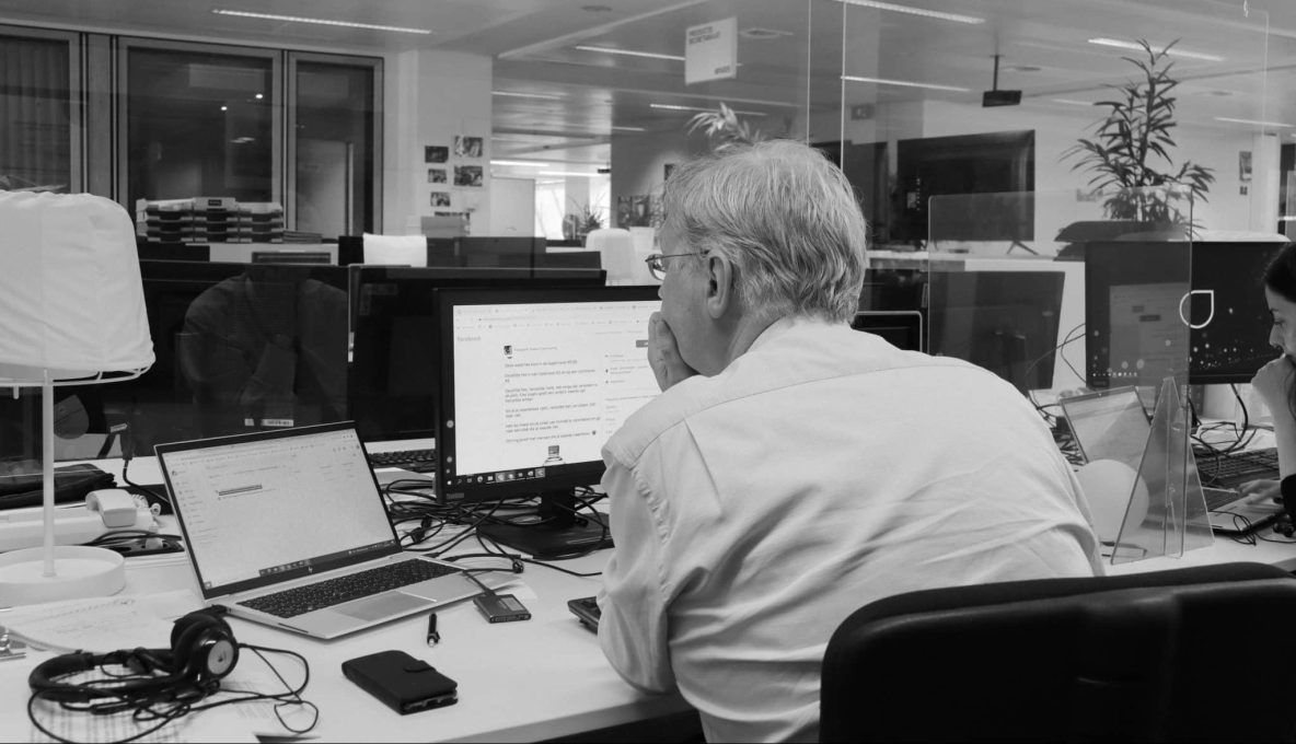 zwart-wit foto van man aan het werk, zittend aan bureau voor een computer.